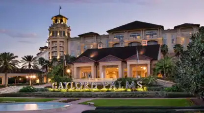Exterior view of the Gaylord Palms Resort at dusk, featuring a well-lit main entrance, a large hotel building, and landscaped grounds with palm trees.